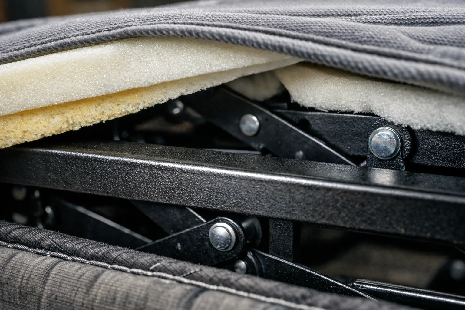 Close-up of a pull-out sofa bed mechanism with thin mattress above a transverse steel support bar