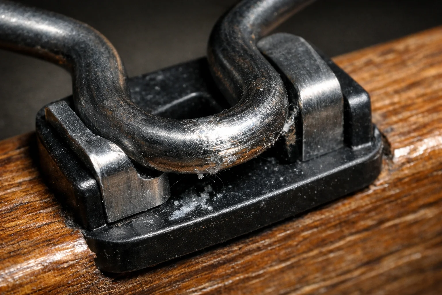 Extreme close-up of a sinuous spring rubbing a misaligned clip on a sofa frame rail, showing scoring and wear