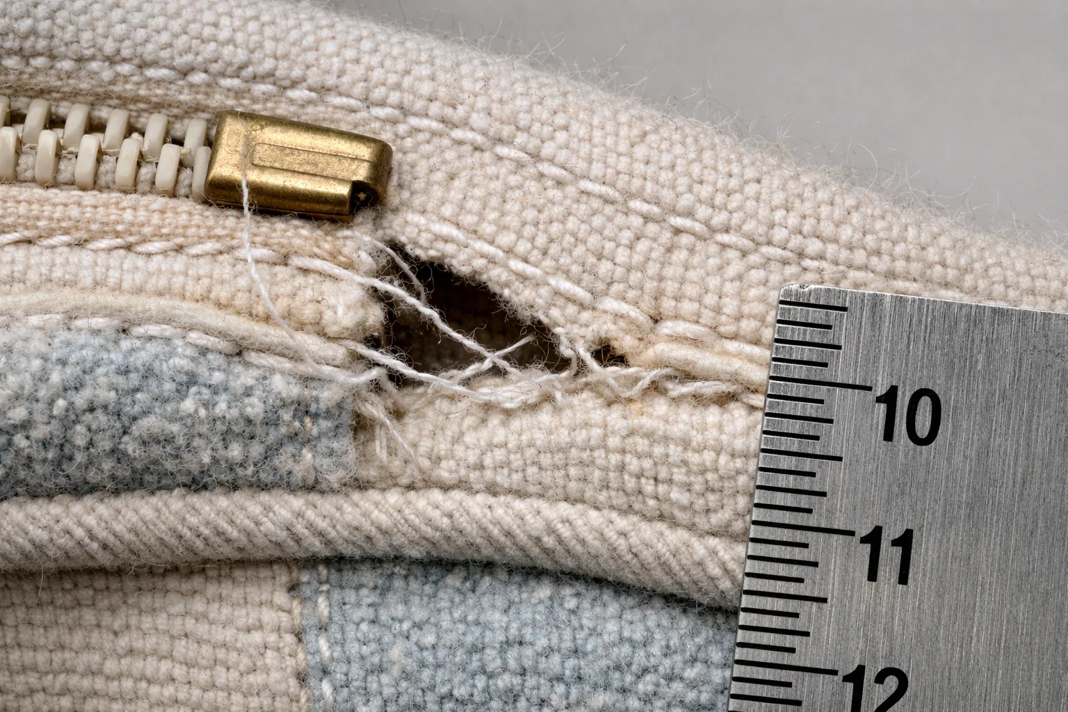Macro view of a cushion cover seam near a zipper showing stitch strain, slight gapping, and distorted piping
